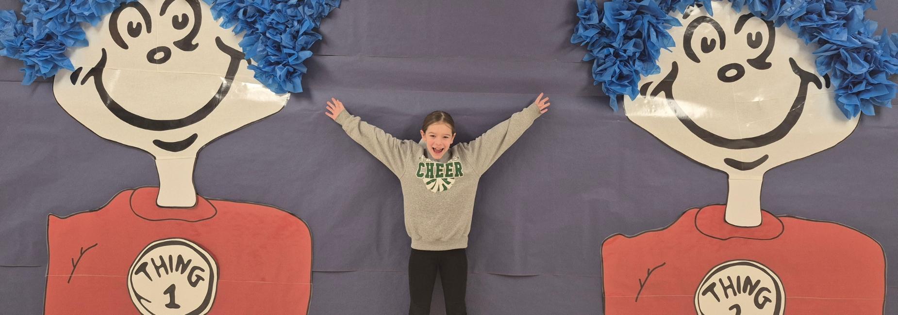 Child smiling with arms outstretched between two large cartoon characters with blue hair.