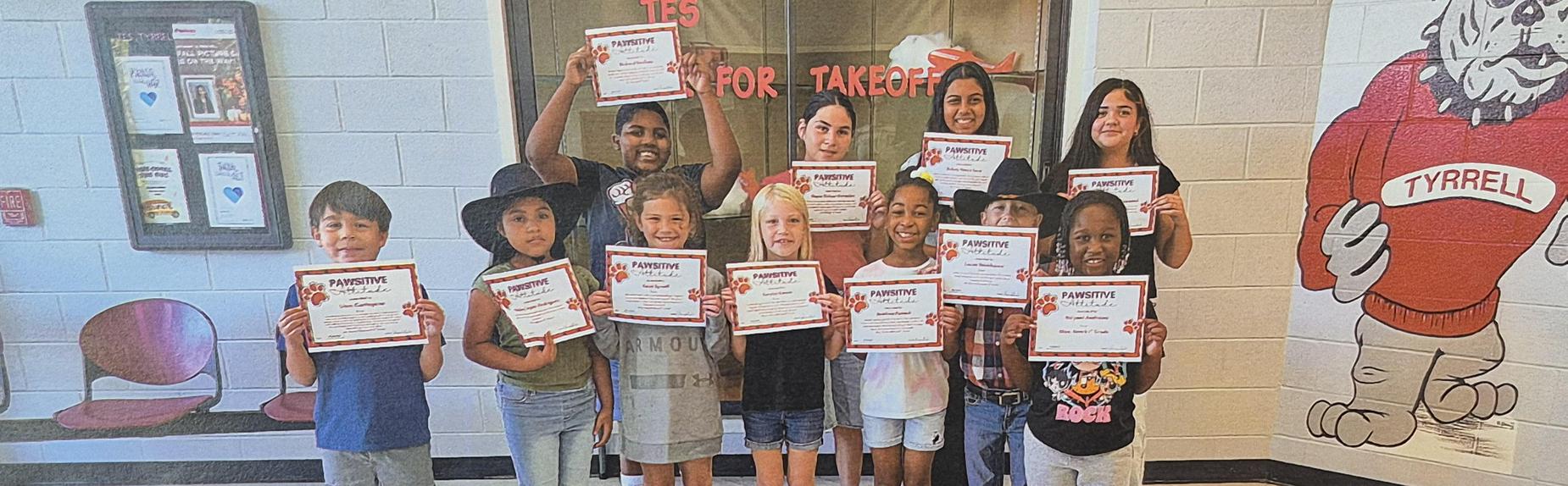 Children holding certificates in a school hallway.