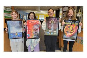 four students holding framed pictures of book covers