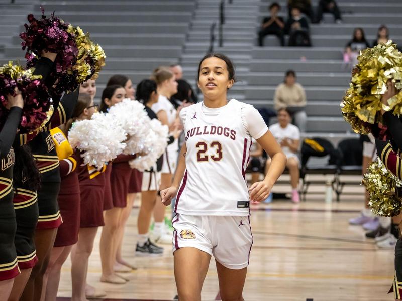 Teenage girl in sports uniform running through a cheerleader tunnel during a basketball game.