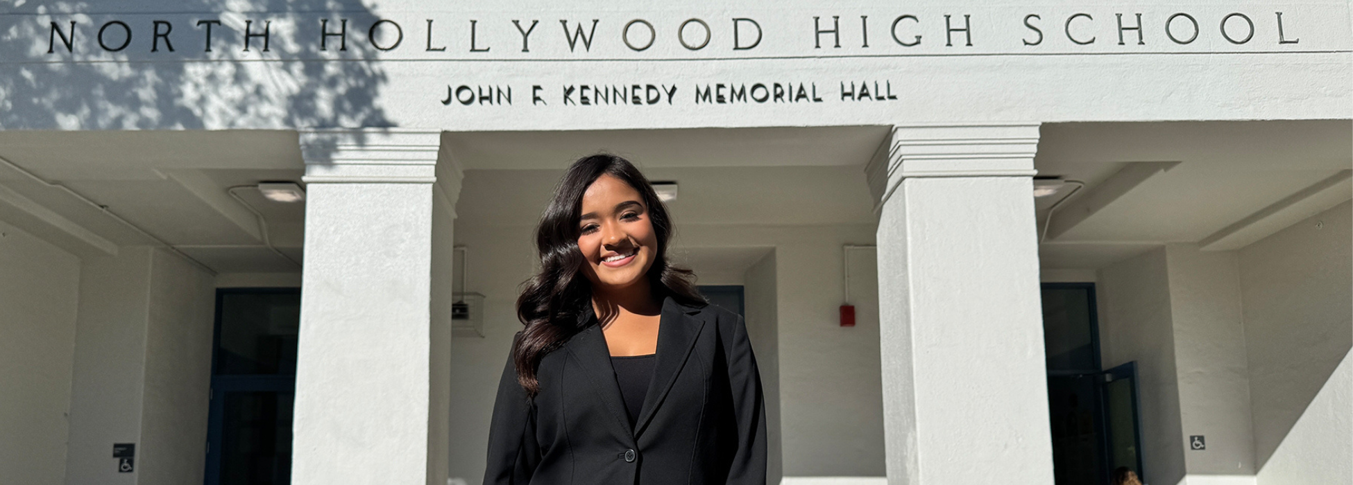 A student in a black suit stands in front of North Hollywood High School.
