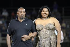 A man and a woman in a formal dress walking together on a football field.