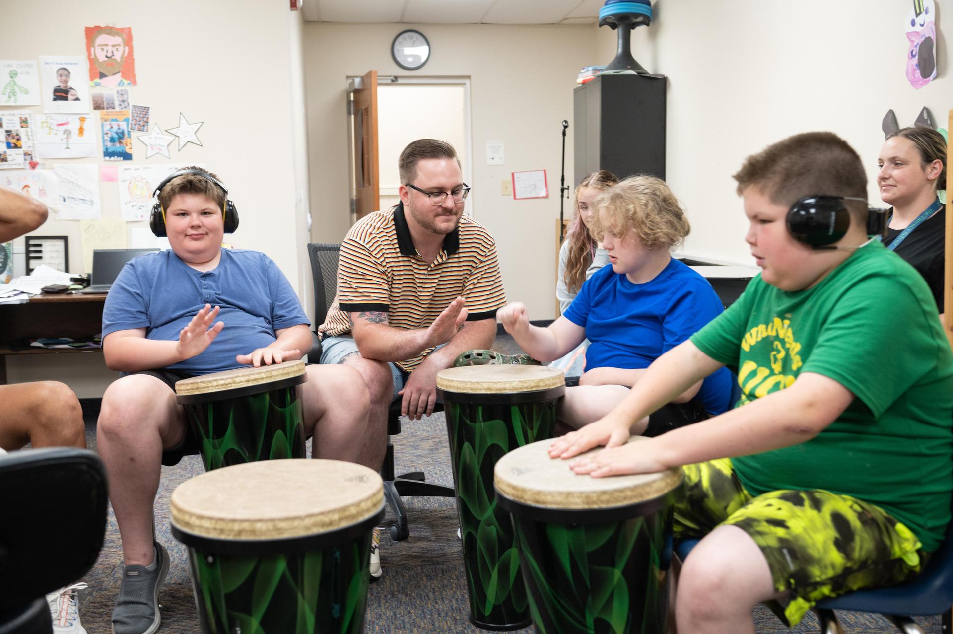 A music therapy session with children playing drums and a facilitator.