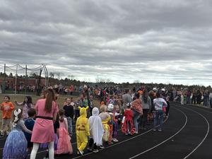A large group of children in costumes lined up on a track under a cloudy sky.