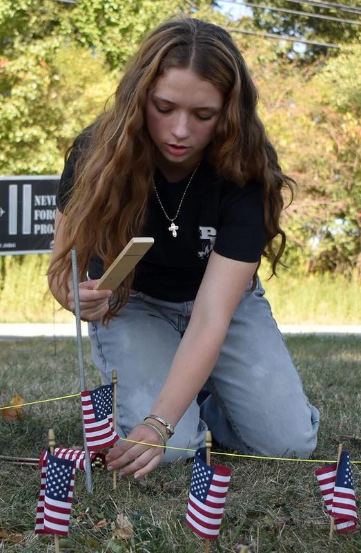 A girl carefully arranges small flags while kneeling on the grass.