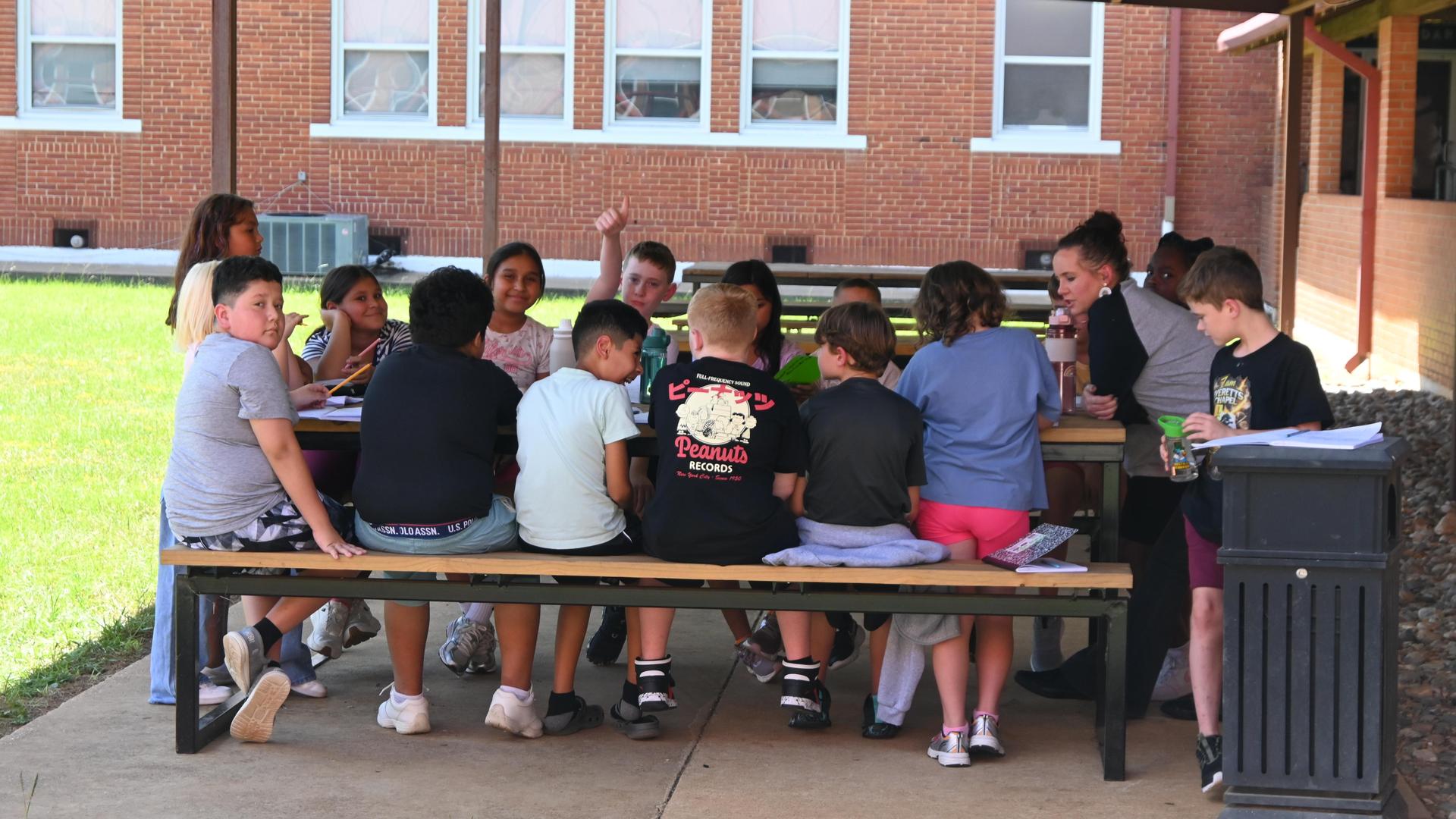 A group of children and adults gathered around a picnic table outdoors.