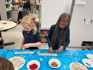 second grade girls using cement and mosaics to decorate their menorahs and hold the casings in place.