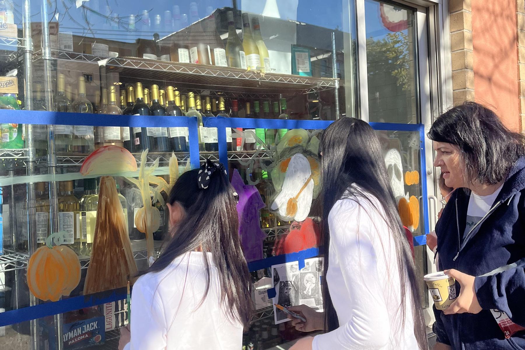 Women and girls adding colorful art to a shop window.