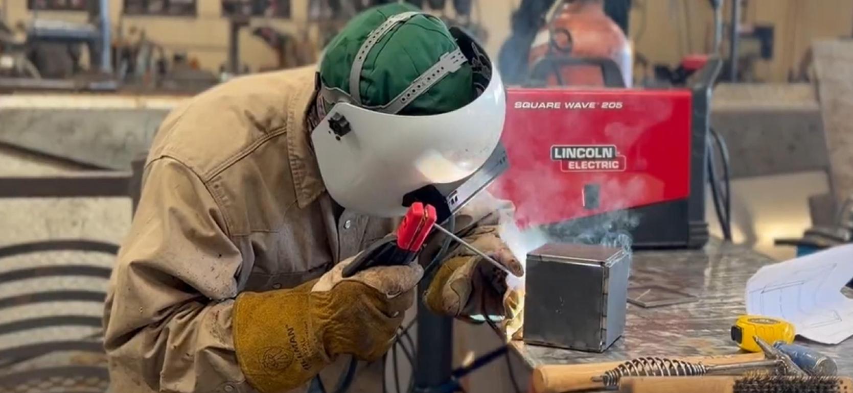 Welder using a welding machine with protective gear in a workshop.
