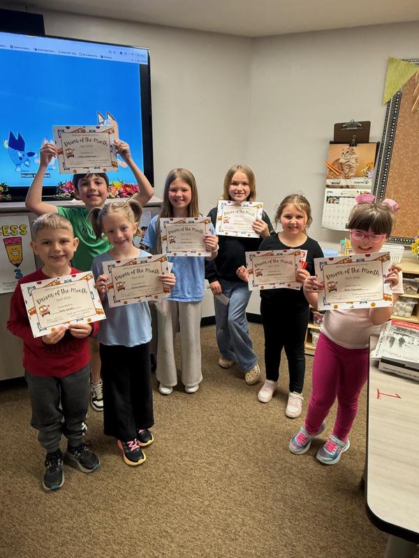 Seven kids holding 'Student of the Month' certificates in a classroom.