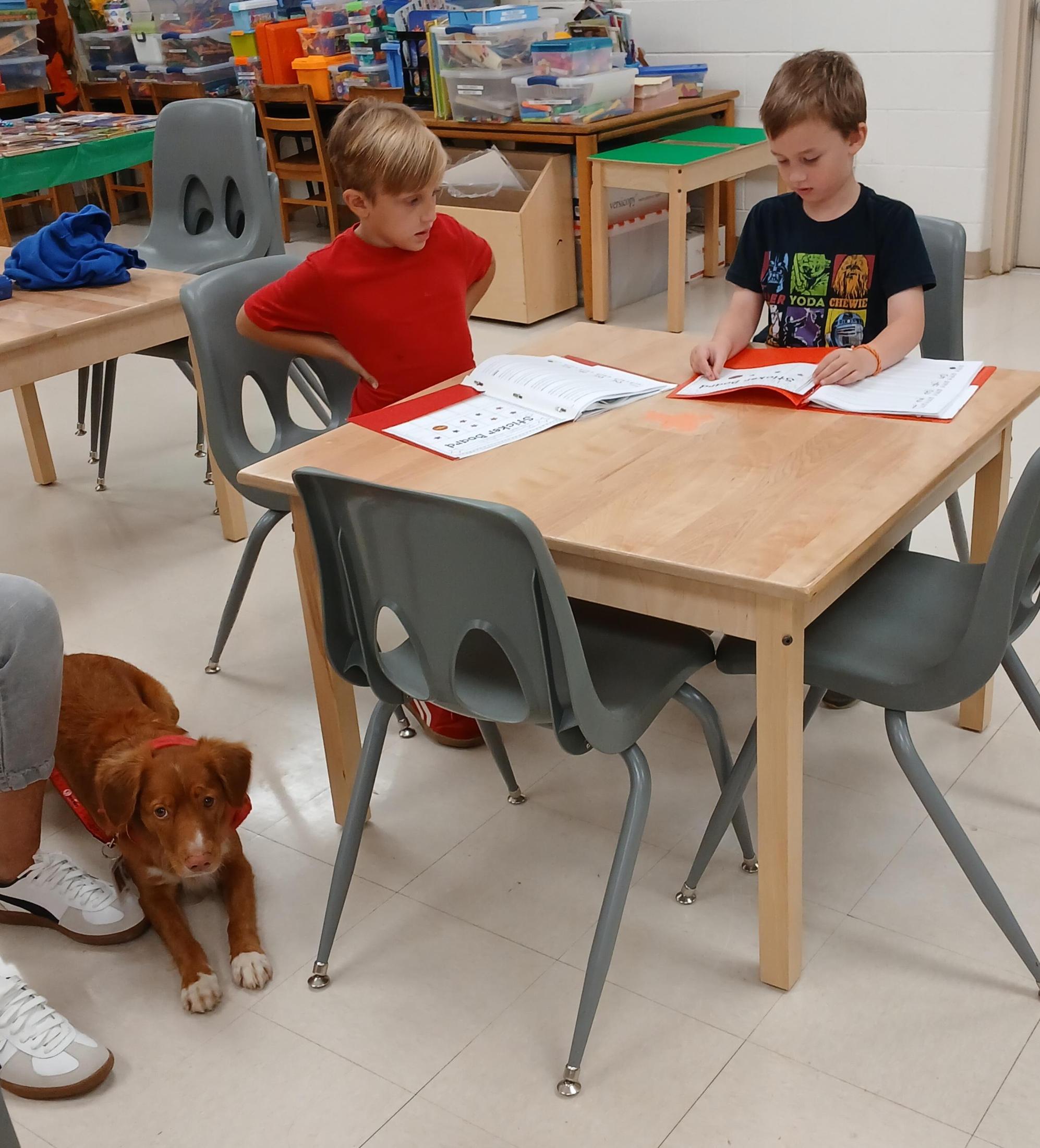 Students reading with a dog in the library at a table 