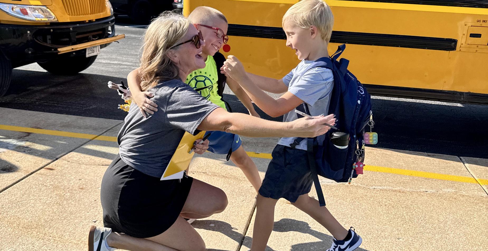Students greet a teacher with hugs on the first day of school.