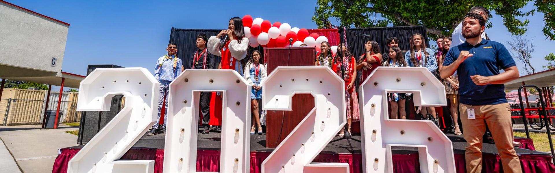 Graduation ceremony scene with students celebrating in front of 2020 display.