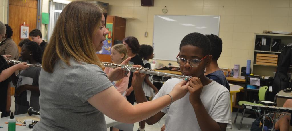 teacher helps boy blow into a flute