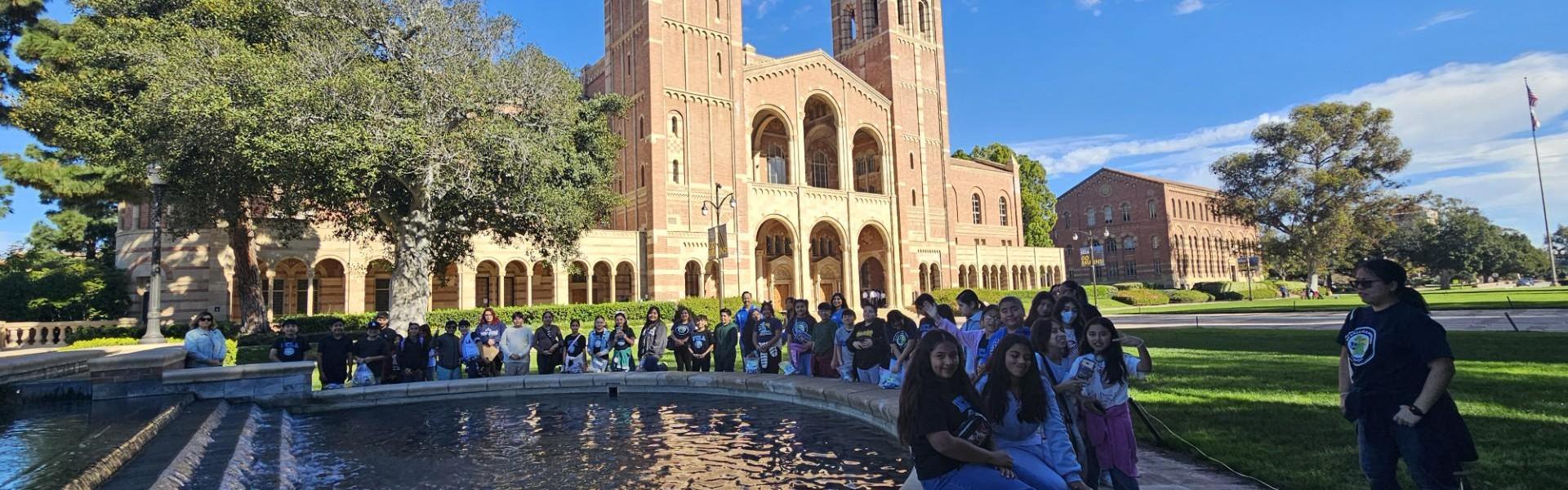 Group of students posing near a fountain with a campus building in the background.