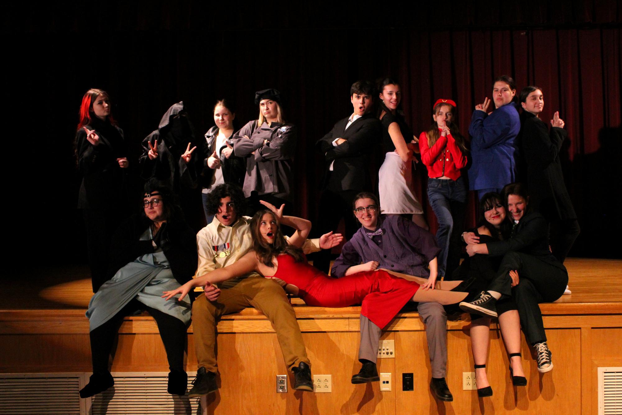 Group of people in costumes posing on stage, showing various expressions and outfits.