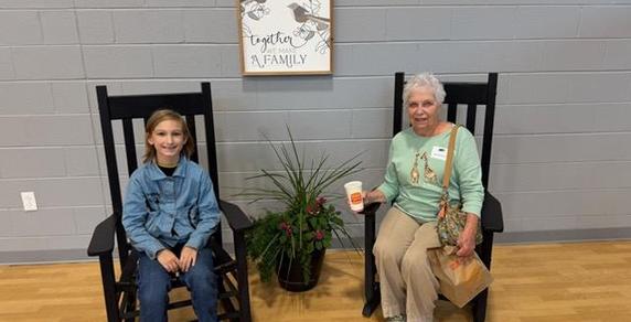 A boy and an elderly woman sitting in rocking chairs with a wall sign above them.
