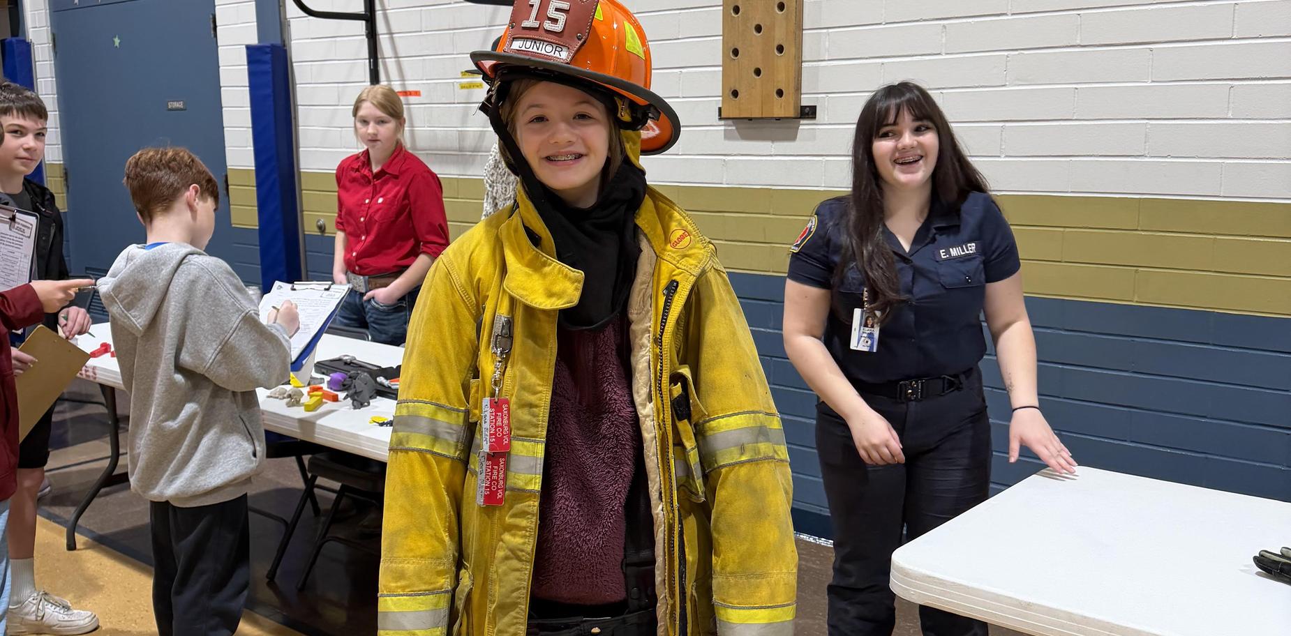 Young girl in firefighter gear smiling at an event with a group of people behind her.