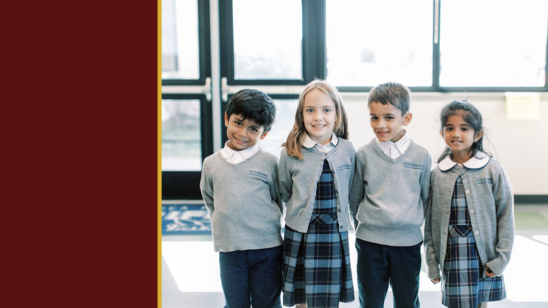 Four smiling young students in gray sweaters stand by windows