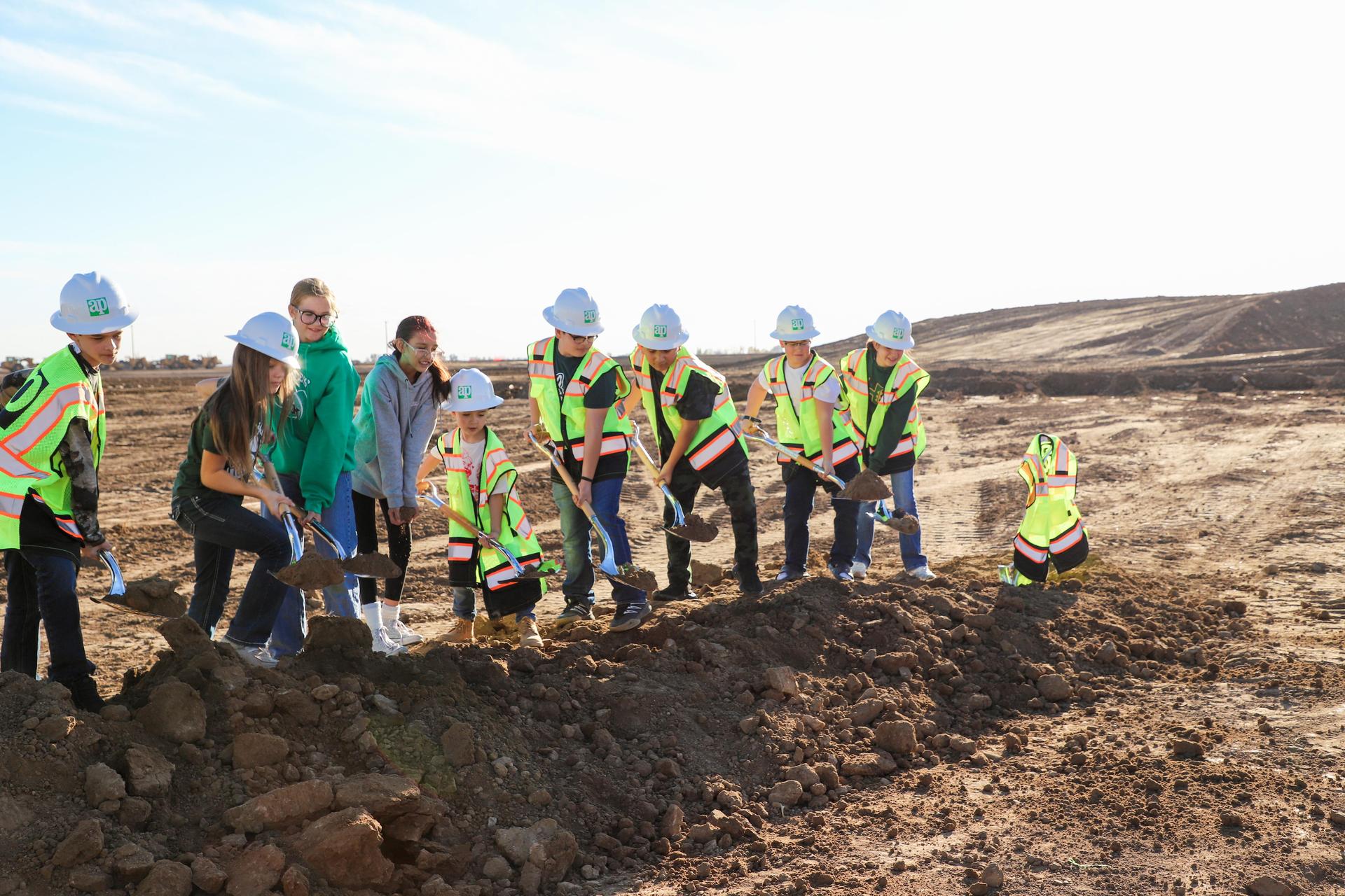 Group of people in vests excavating a site under a clear sky.