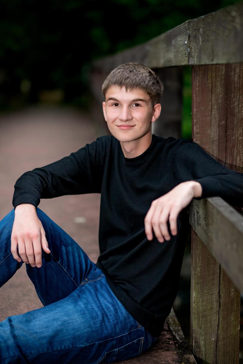A student sits on a bridge, posed for their senior photo