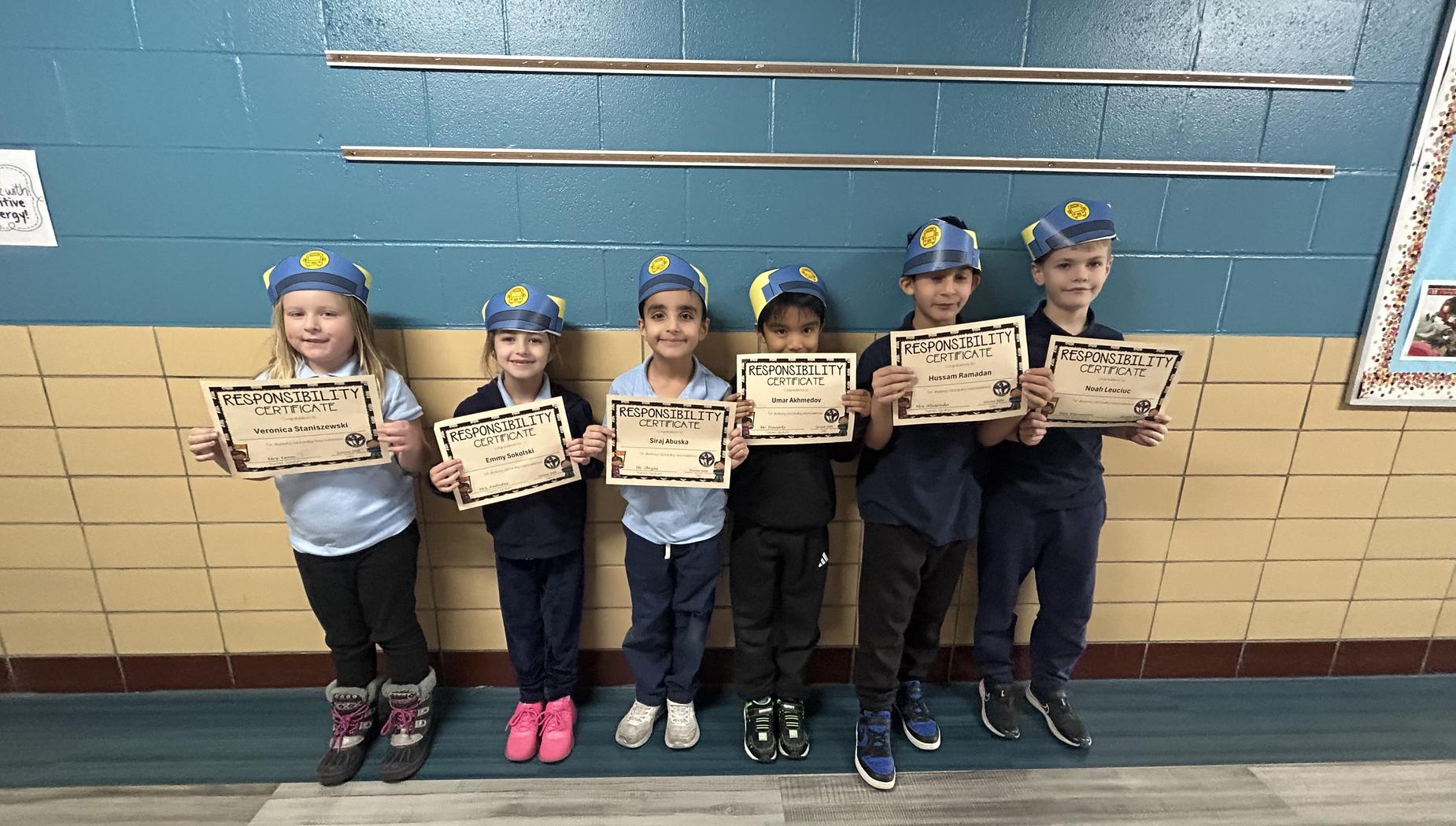 Six children in blue hats holding responsibility certificates, smiling for the camera.
