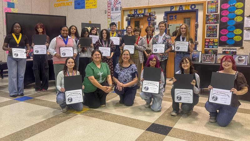 A group of students and teachers smiling and holding awards