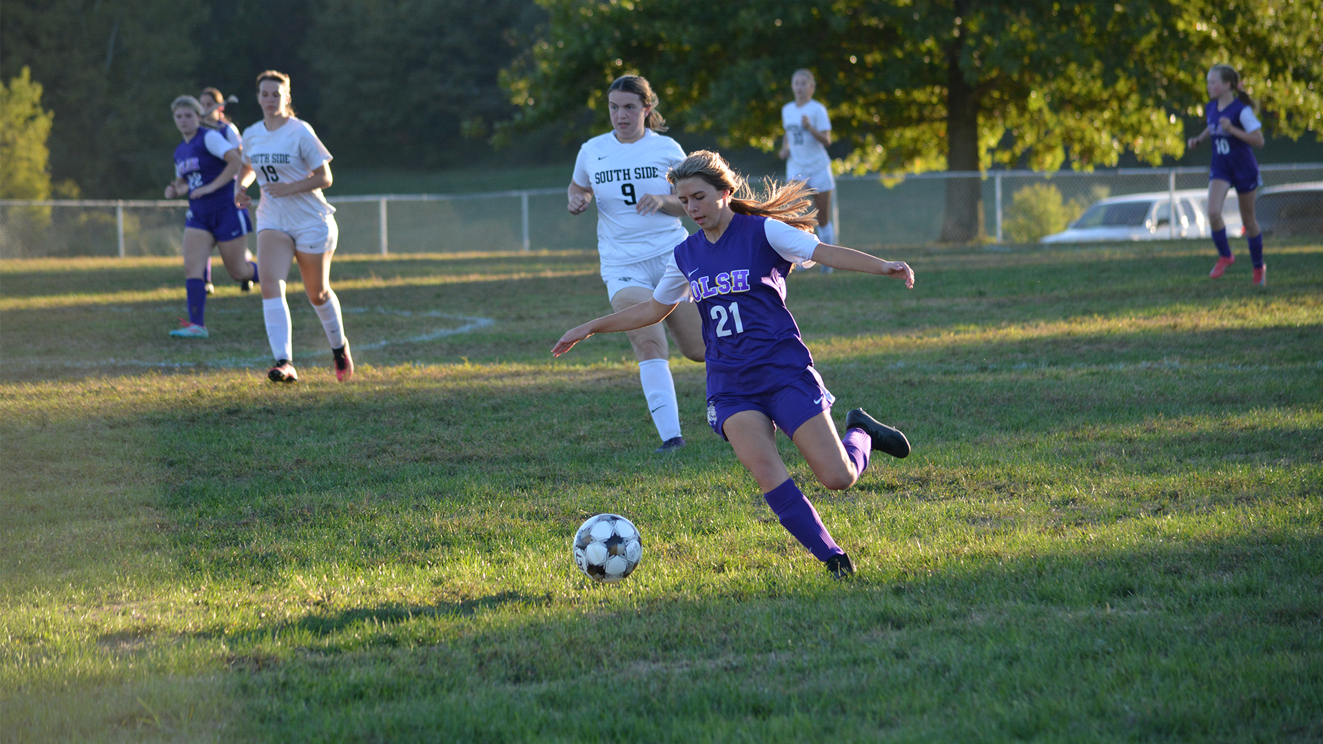 girls soccer player in purple uniform about to kick the ball as opposing team players approach