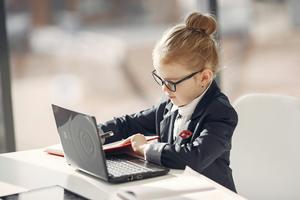 Young child with a blonde bun wears a suit and works on a laptop