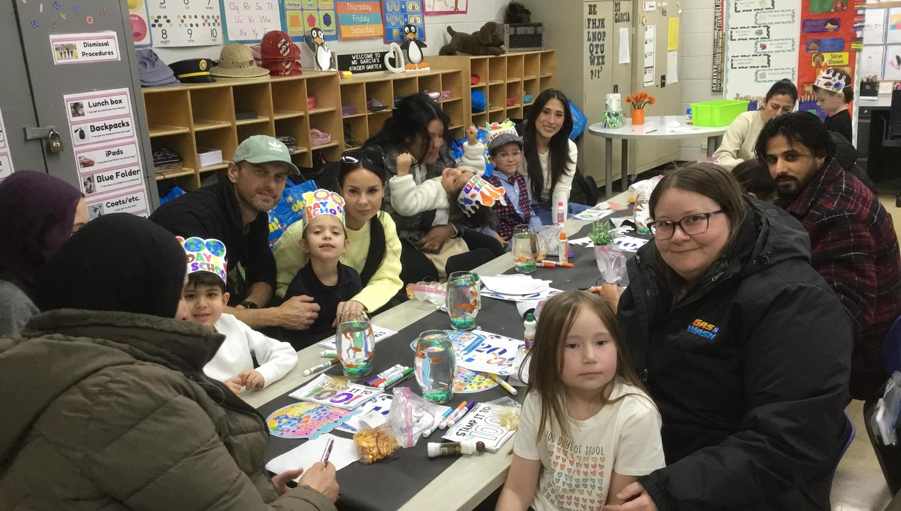 Group of adults and children at a table, celebrating with colored hats and crafts.