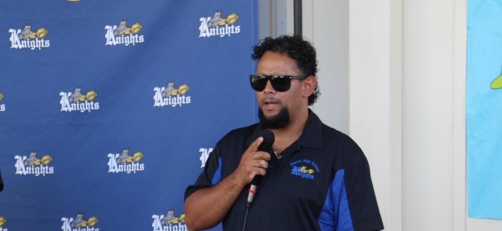 A person speaking at a podium with a blue Knights banner in the background.