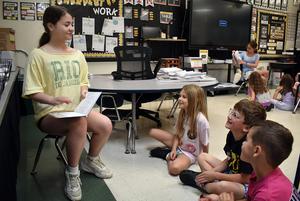 A student reading to a group of engaged children in a classroom.
