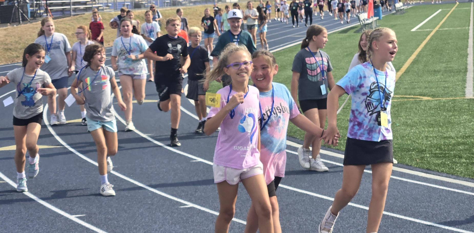 Children running and enjoying a track event, wearing colorful shirts and smiles.