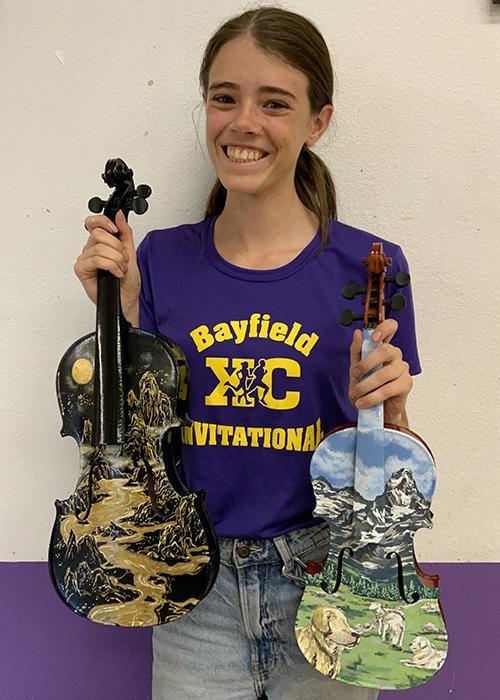 A girl holds up two painted violins.
