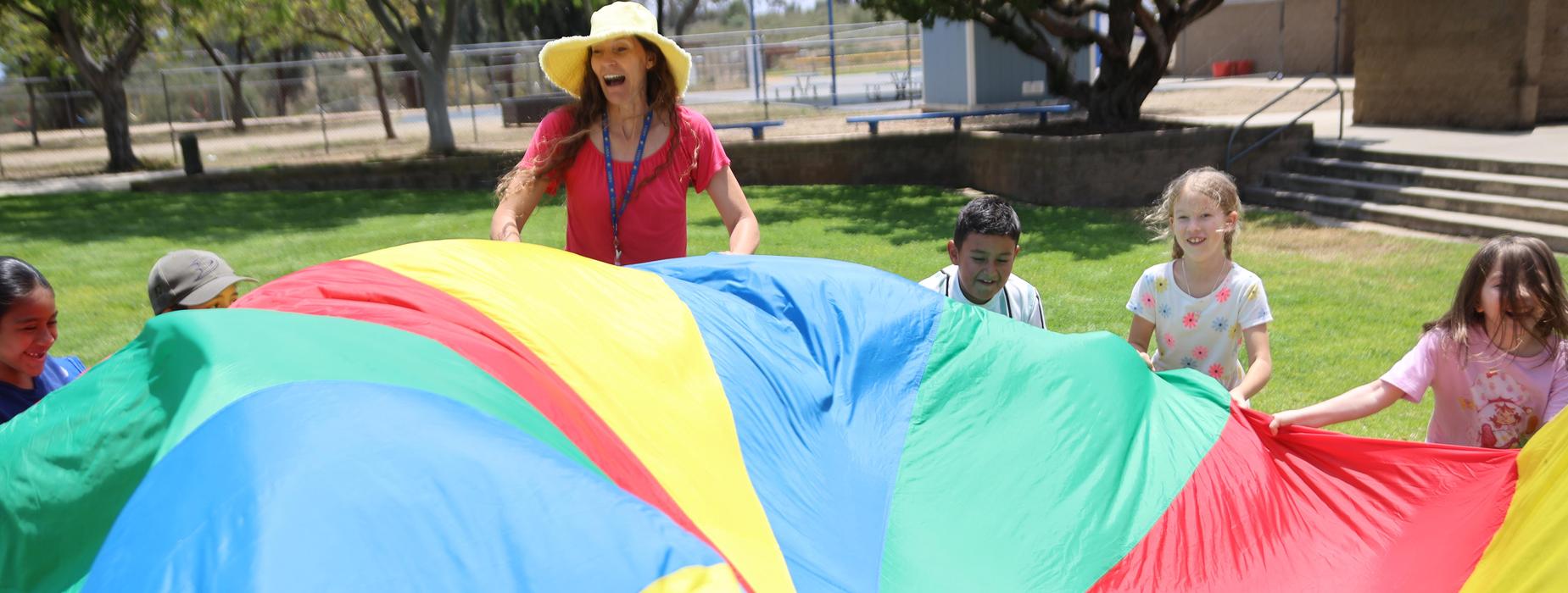 Children playing with a large colorful parachute outdoors.