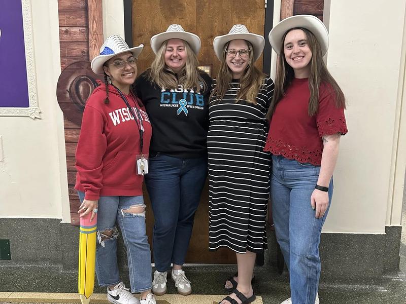 Four women wearing hats and posing together in a hallway.