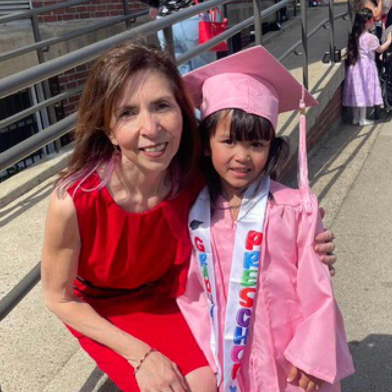 A woman in a red dress poses with a girl in a pink graduation cap and gown.