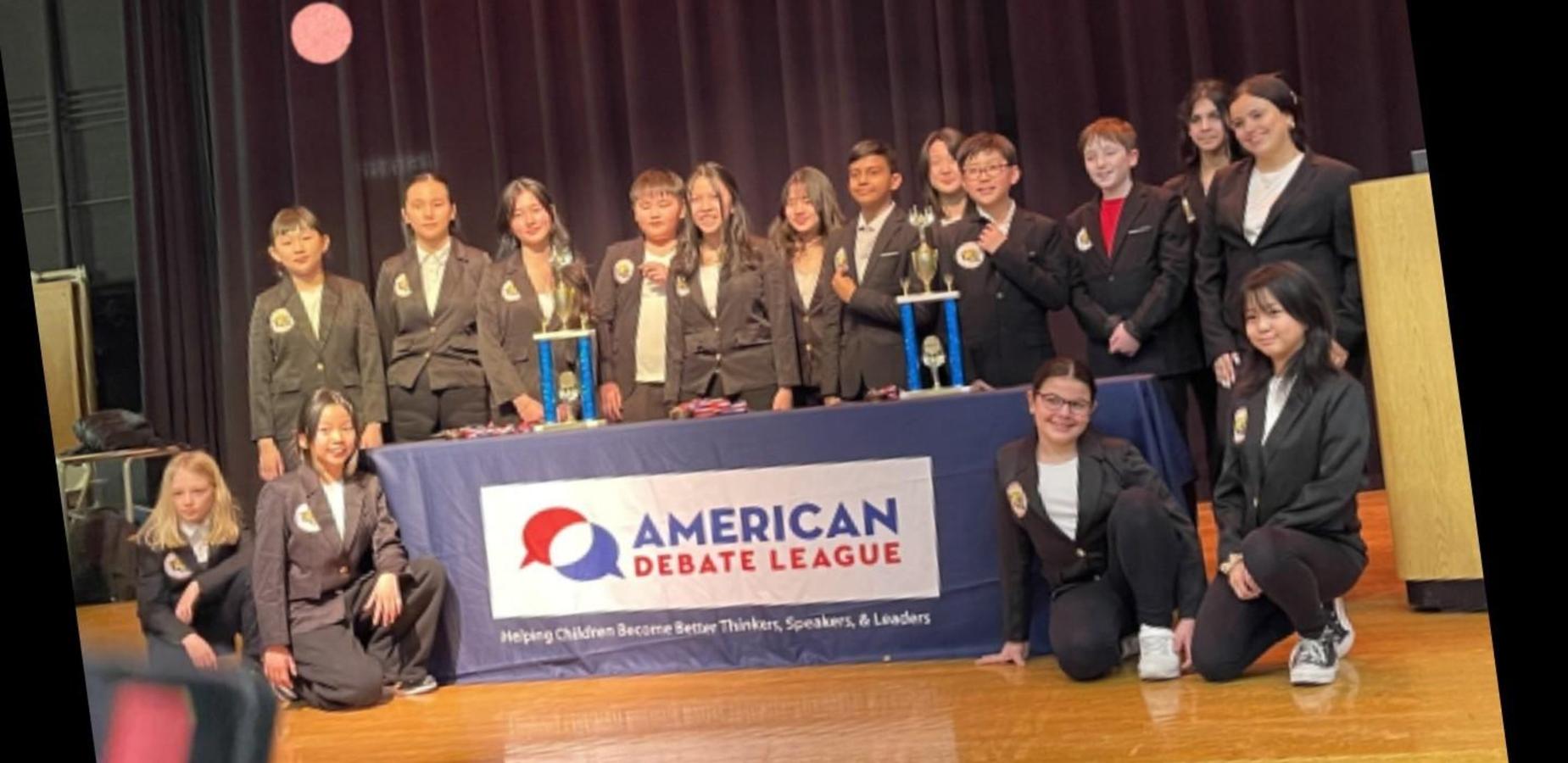 Group of students in formal attire at a debate event with trophies.