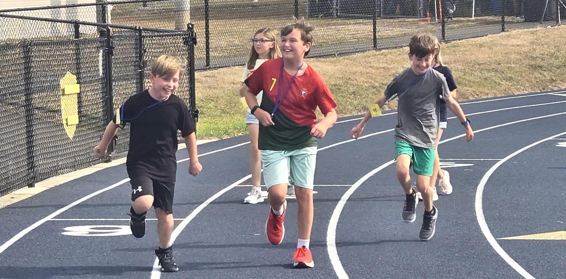 Children running joyfully on a track during a sporting event.