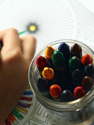 Jar of crayons with a hand coloring on a page.