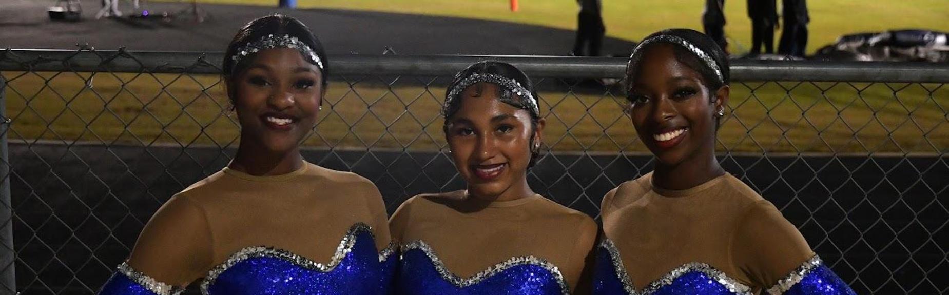 Three dancers posing together in sparkly blue costumes with nude accents.