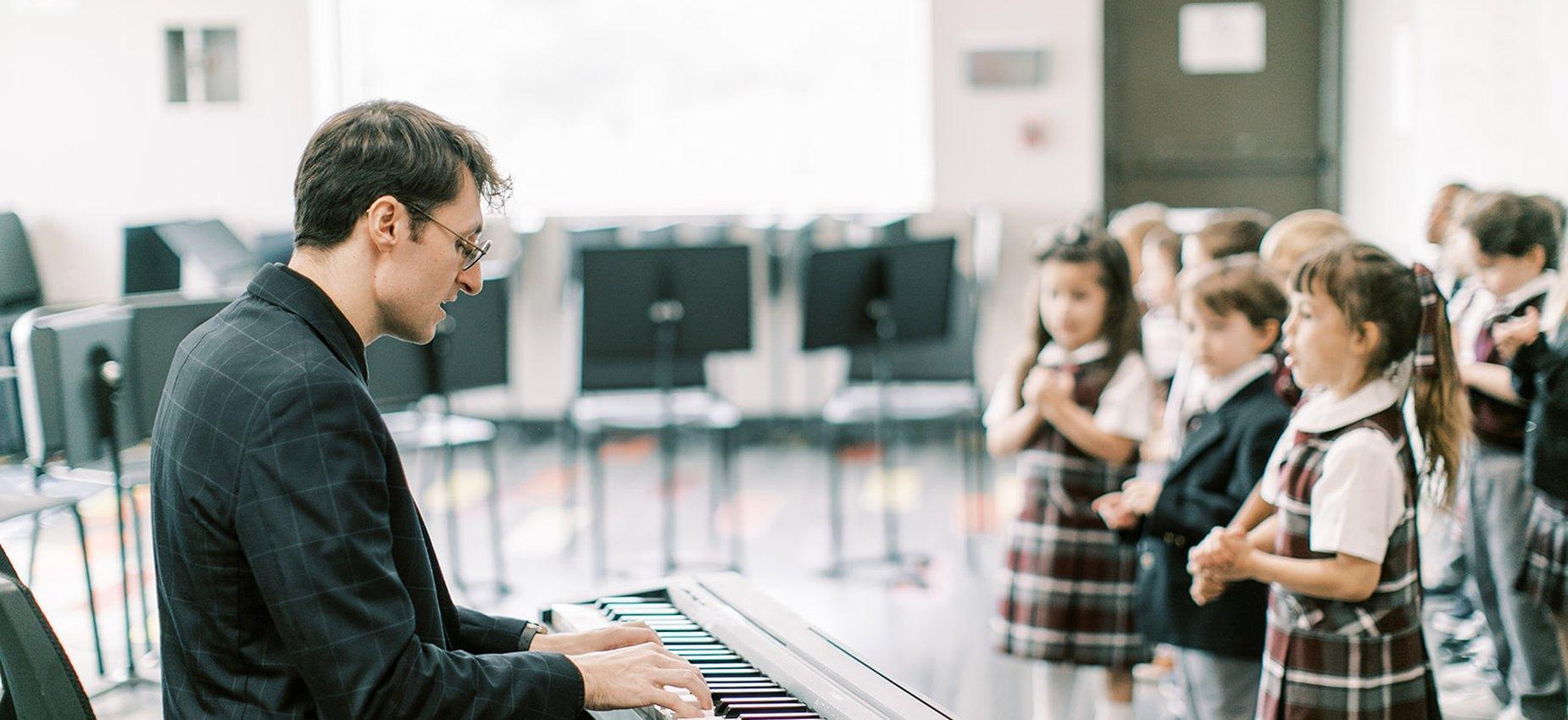 Music teacher at the piano leading young students in song at El Paso Classical Academy
