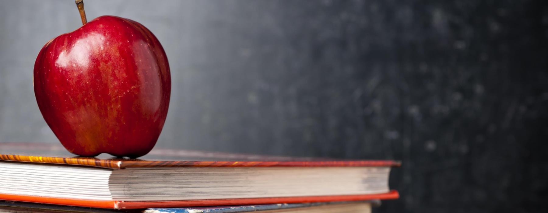 Red apple on stacked books with a dark background.