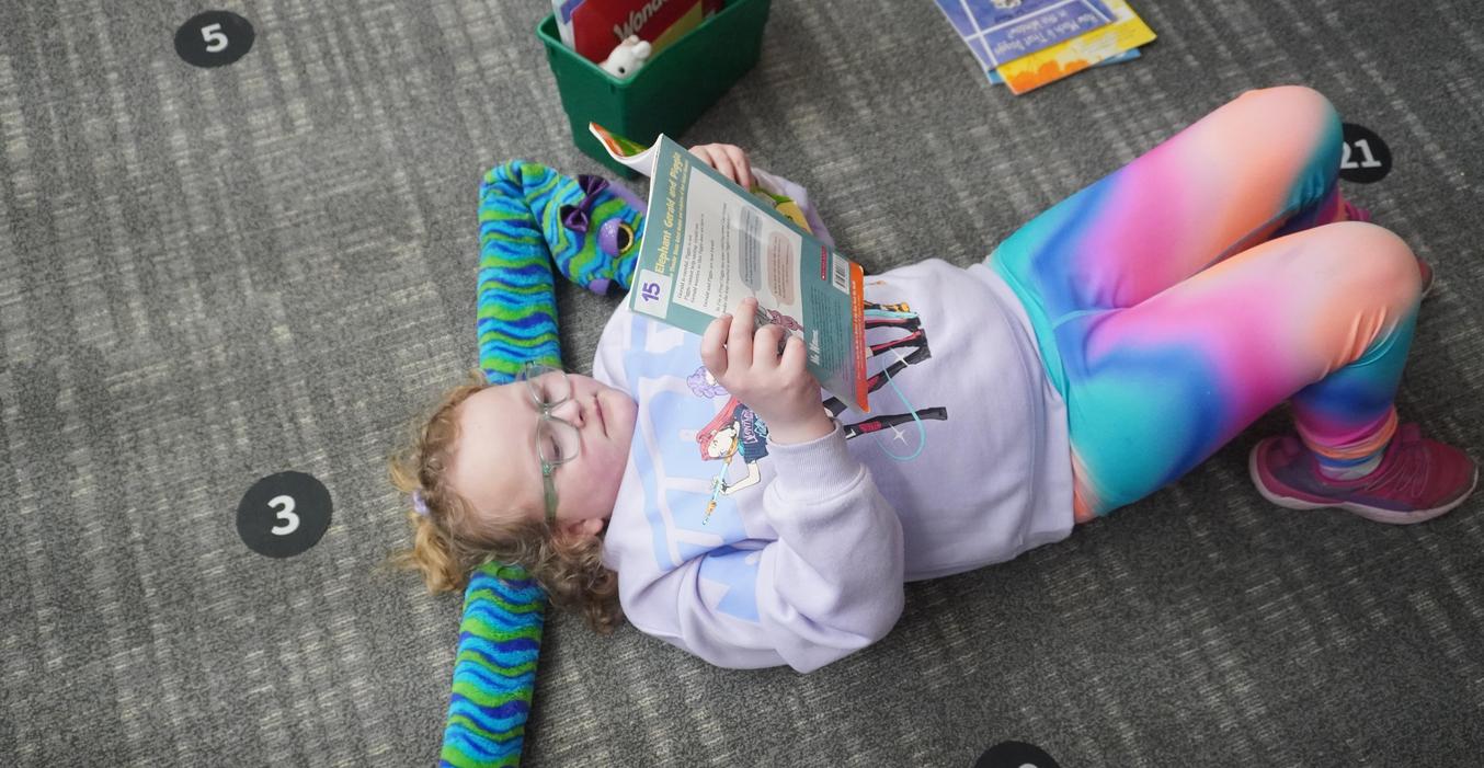A student lays on her stuffed animal while she reads a book.
