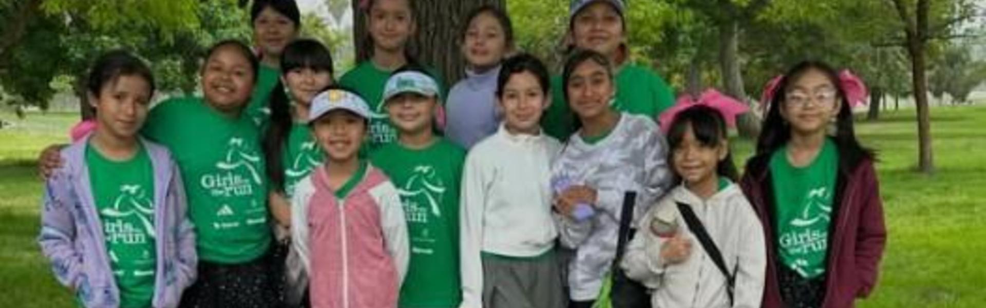 Group of girls in green t-shirts posing together outdoors in a park.