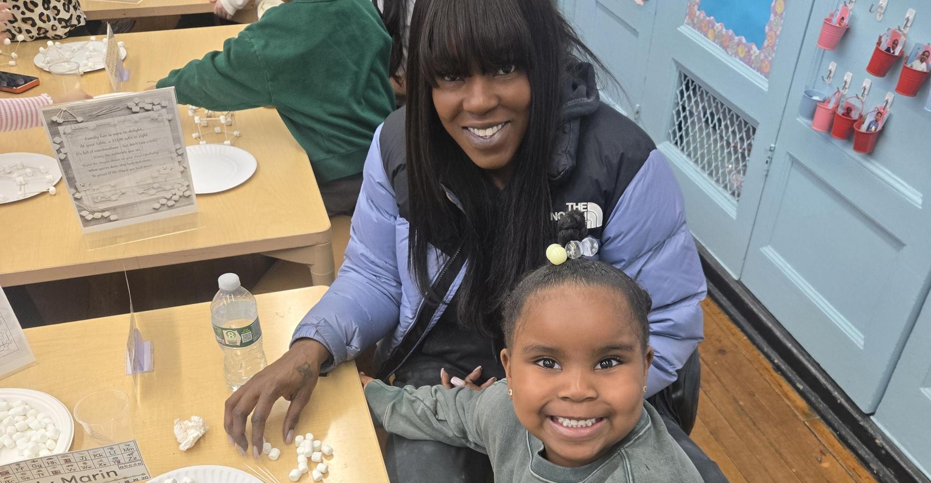 A woman and a young girl smiling together at a table with craft supplies.