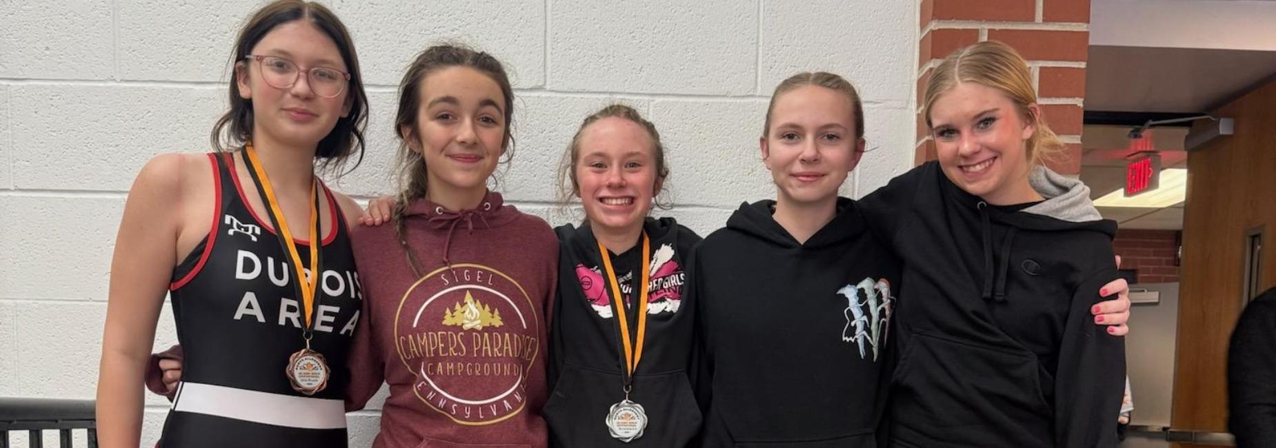 Five girls pose together, smiling and wearing medals at a school event.