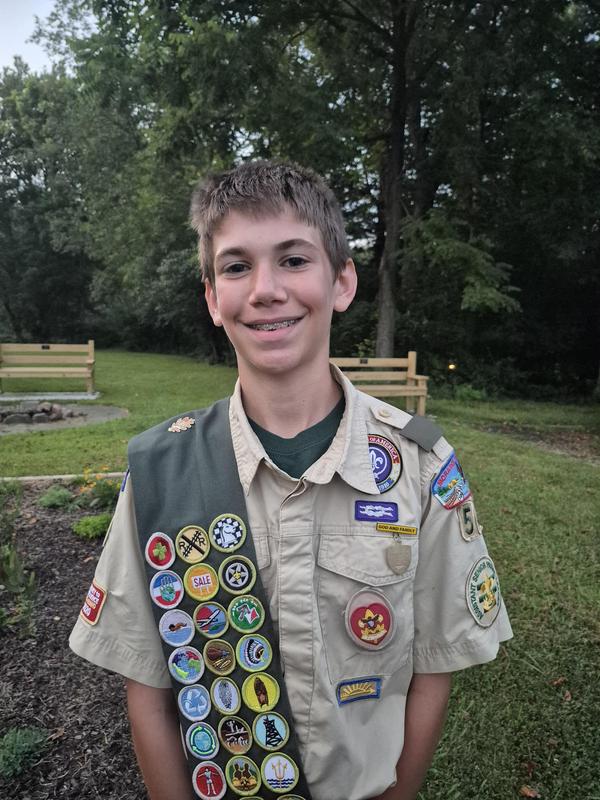 boy scout in uniform in front of garden and benches he did for his project