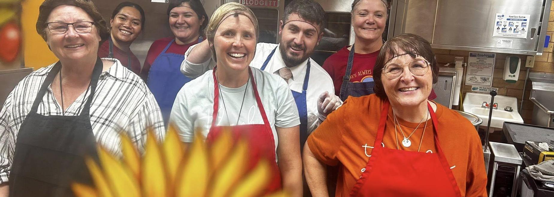 Group of smiling kitchen staff posing together behind a counter.