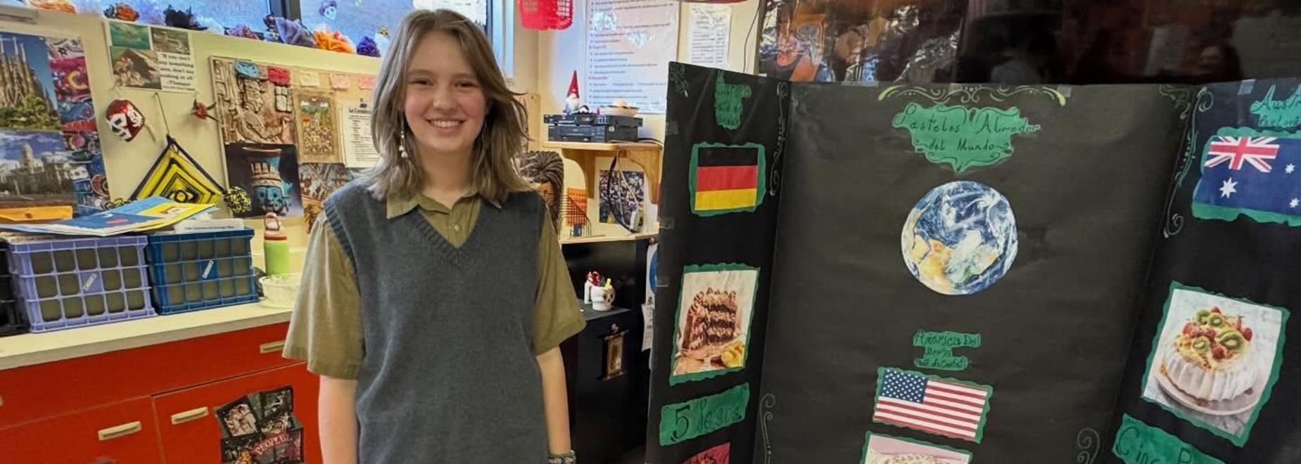A girl stands beside a project board featuring international desserts.